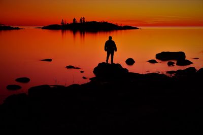 Silhouette people standing on rock against sky during sunset