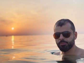 Close-up portrait of man in sea wearing sunglasses against sky during sunset