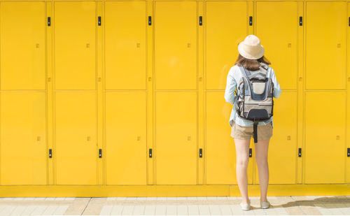 Rear view full length of woman standing against yellow lockers