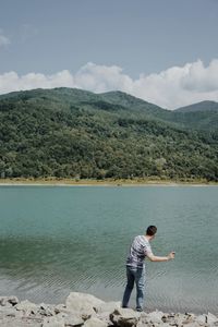 Rear view of man standing by lake towards mountain