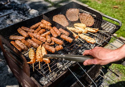 Cropped hand of man preparing meat on barbecue grill