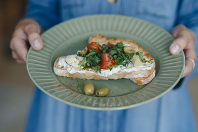 Midsection of businesswoman holding bruschetta while standing in cafe