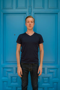 Portrait of young man standing against blue door