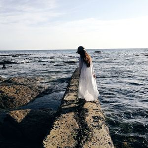 Rear view of young woman standing at beach against sky