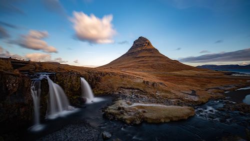 Scenic view of waterfall with mountain in background against cloudy sky