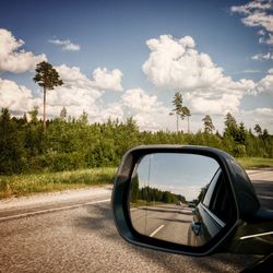 Side-view mirror of car on road against sky