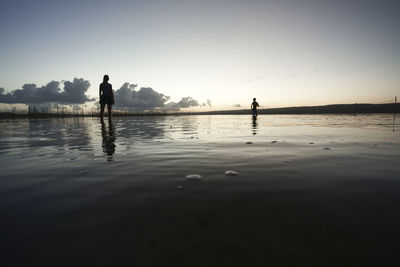 Silhouette people standing in water against sky