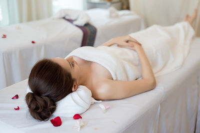 Young woman with flower petals lying on massage table in spa