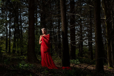 Senior woman with red scarf standing by trees in forest