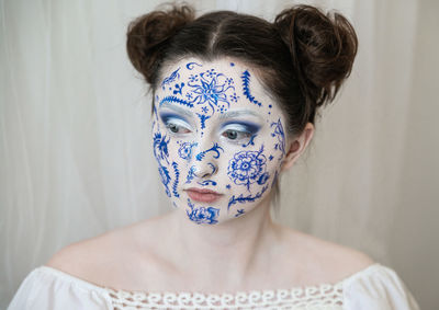 Woman with painted face looking away against curtain at home