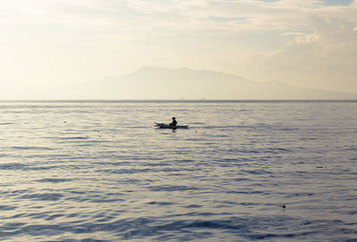 Silhouette man in sea against sky during sunset