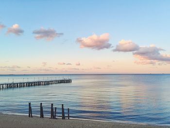 Pier and wooden posts at beach against sky at dusk