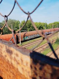 Rusty metal fence by trees against sky