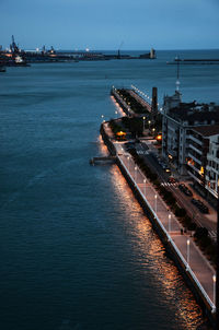 Illuminated city by sea against sky during sunset