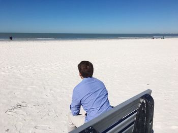 Man sitting on beach at beach against clear sky
