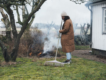 Woman raking and burning branches in garden