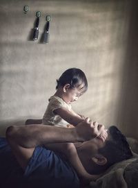 Side view of father playing with daughter while lying on bed at home