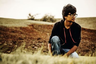 Young man looking away while sitting on land