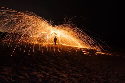 Man spinning illuminated wire wool at beach during night