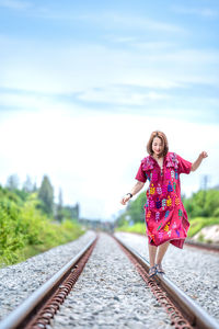 Portrait of woman standing on railroad track against sky