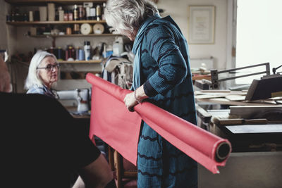 Female owner showing red rolled up fabric to colleagues at workshop