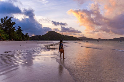 Woman walking on tropical sandy beach at susnset.