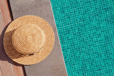 Woman's straw hat lying on the edge of the swimming pool with turquoise water, top view. 