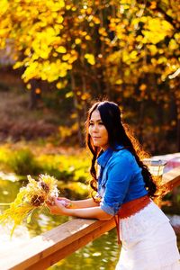 Side view of woman holding flower bouquet while standing by railing