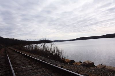 View of railroad tracks by lake against sky