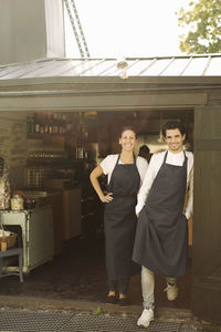 Full length portrait of smiling owners standing outside restaurant