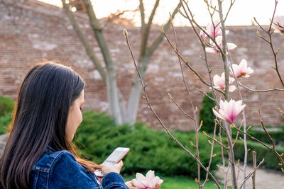 Side view of young woman using mobile phone outdoors