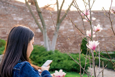 Woman using mobile phone against bare trees in city