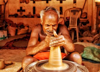 Shirtless senior man making pottery in workshop