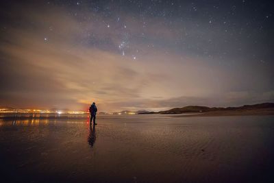 Man walking on sea shore against starry sky