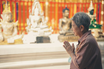 Old asian elder senior woman traveler tourist praying at buddhist temple.