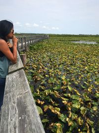 Woman in sunglasses looking at water lily on pond against sky