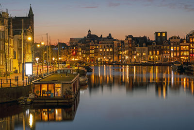 Illuminated buildings by river against sky at dusk