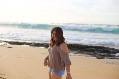 Portrait of smiling woman standing on beach against sky