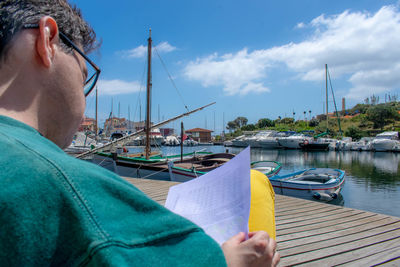 Midsection of man holding camera at harbor against sky