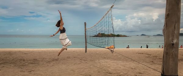 Side view of woman playing beach volleyball against cloudy sky