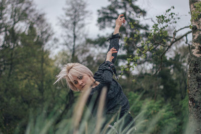 Portrait of young woman with arms raised in forest