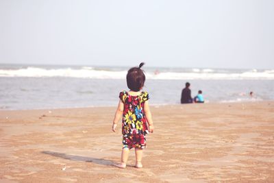 Rear view of boy walking on beach against clear sky