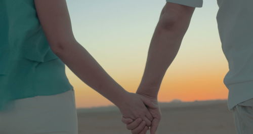 Midsection of man and woman standing against sky during sunset