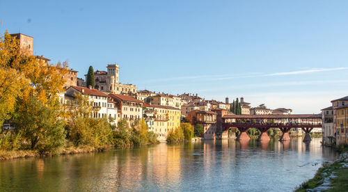 Bridge over river by buildings against clear sky