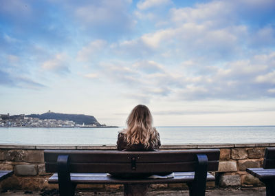 Rear view of woman sitting on bench against sea