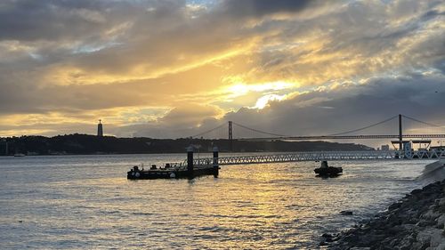 Silhouette bridge over sea against sky during sunset