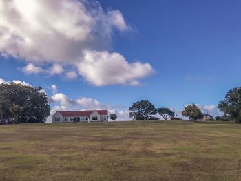 Scenic view of field by houses against sky