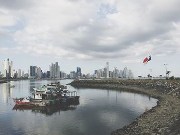 Boat moored at lake by city against sky