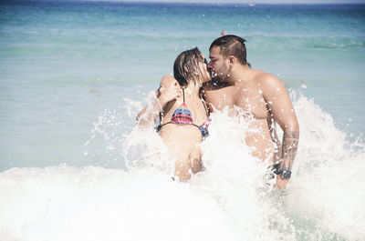 Rear view of people enjoying splashing water at beach
