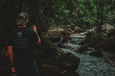 Rear view of man standing by rocks in forest